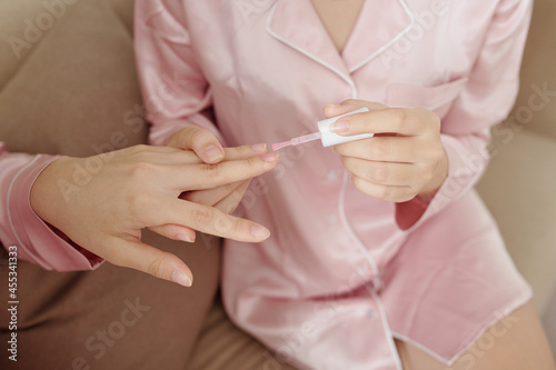 Hands of woman applying transparent base on nails of her friend when they are doing manicure at home