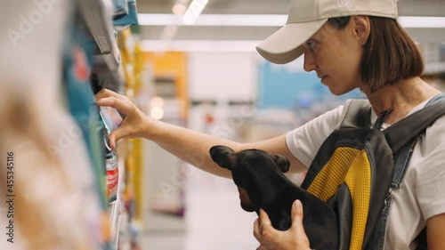 Young woman shopping at the supermarket with little toy terrier dog in her hands. She choosing dog food for her pet. High quality 4k footage photo