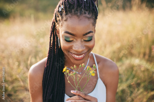 Beautiful black young woman in the park portrait long braids smiling flower bright makeup closeup