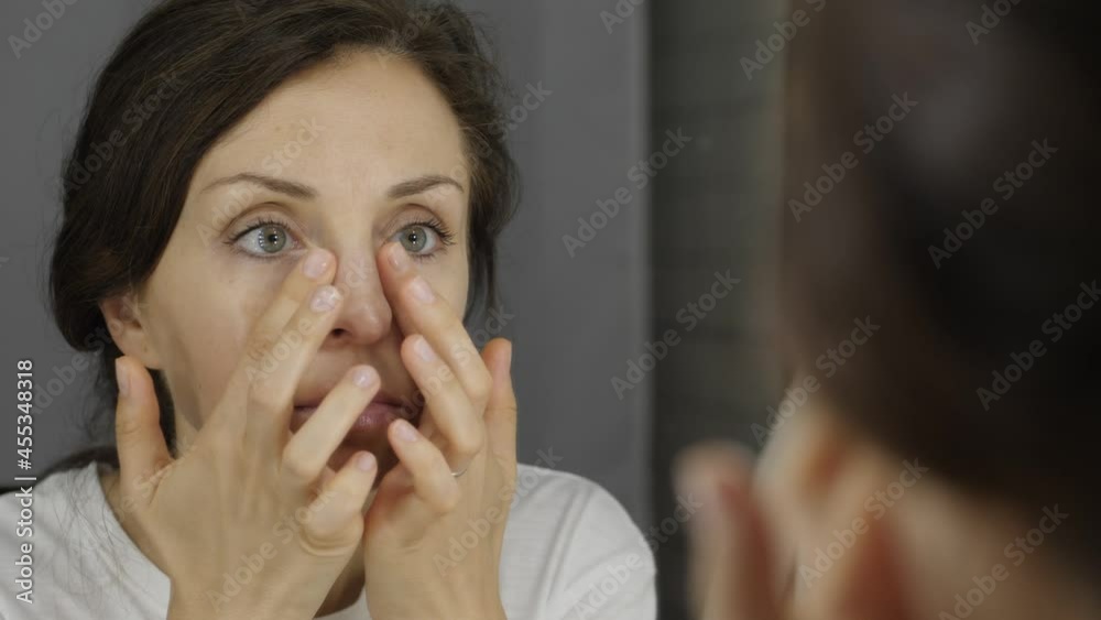 Rear back view serious beautiful 30s woman is applying facial moisturizer cream while looks in the mirror reflect. Skincare, professional care product cosmetics advertisement concept. Rear back view serious beautiful 30s woman is applying facial moisturizer cream while looks in the mirror reflect. Skincare, professional care product cosmetics advertisement concept.