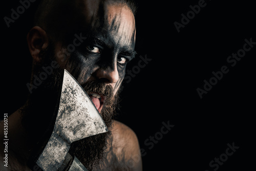 Viking warrior with black war paint, licking his axe. photo