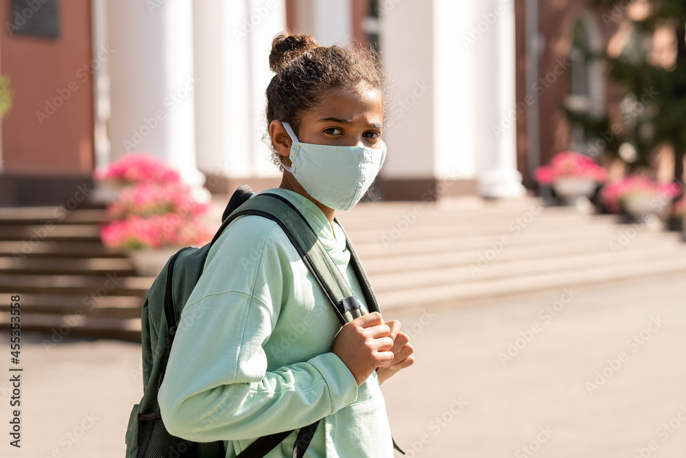 Cute mixed-race schoolgirl in casualwear and protective mask going to school in the morning Cute mixed-race schoolgirl in casualwear and protective mask going to school in the morning