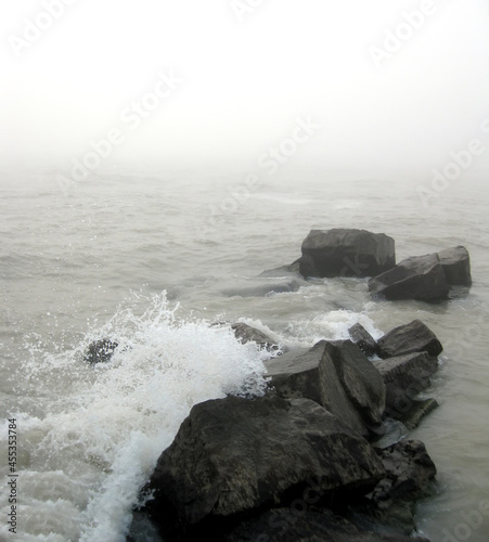 FOGGY WAVES Rocks near the shore being hit by the waves on a foggy day.
