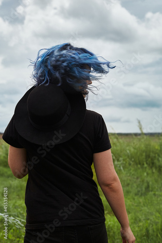 Attractive woman with blue hair with black hat dancing outdoors. Dreamy portrait young lady. Concept of freedom, well being and lifestyle