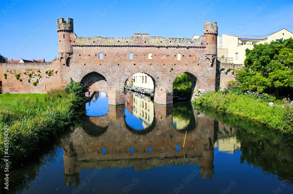 View over water canal on medieval watergate stone wall with 3 arches from 14th century with reflection against blue summer sky - Zutphen (Berkelpoort), Netherlands
