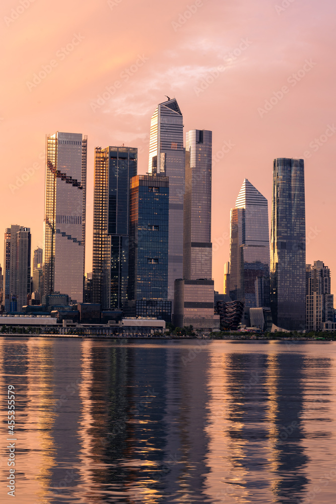 New York, NY - USA - Vertical image of the skyline of westside of midtown Manhattan at sunrise, with reflections seen in the Hudson River. Highlighting the Hudson Yards complex