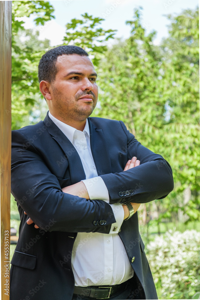 Attractive young man in business suit and tie stands with his arms crossed over his chest. Portrait of a successful businessman of Middle Eastern appearance. Man looks into the distance thoughtfully