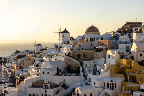  Whitewashed houses and windmills in Oia in warm rays of sunset on Santorini island. Greece