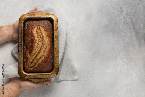 Ready banana bread in a rectangular baking dish in the baker's male hands on a light background