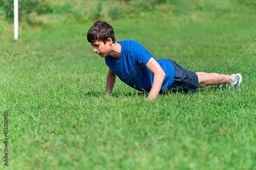 teenage boy exercising outdoors, sports ground in the yard, he does push-ups on the green grass field, healthy lifestyle
