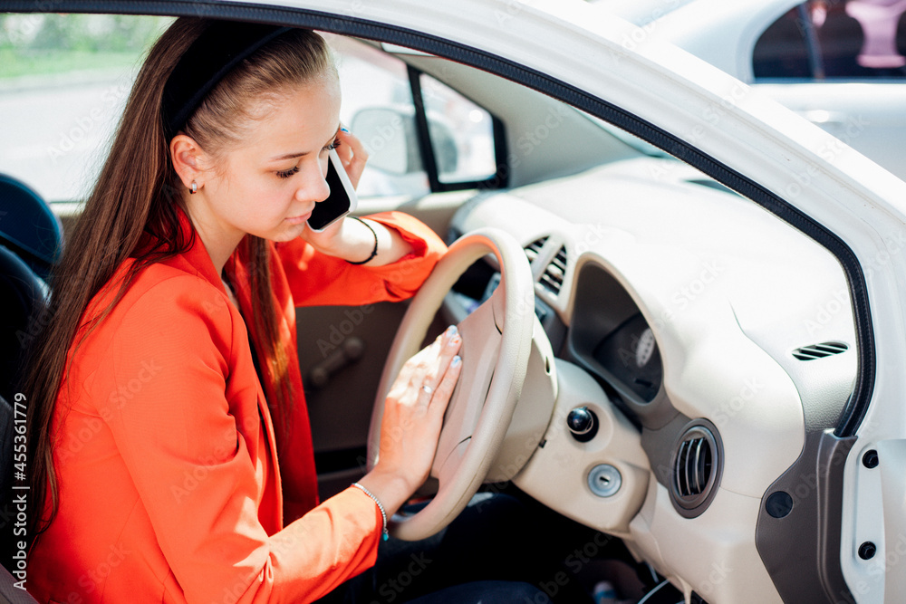 A young woman is sitting at the wheel of a car and talking on a mobile phone. Transport management.