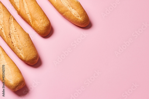 Принти на полотні Four baked artisan whole baguettes with golden crusty floury texture on pink background with copy space