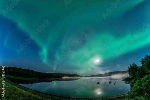 Aurora borealis  Northern green lights with full moon and stars in the night sky over mountain lake  mirrored reflection in water  night mist. Joesjo  Lappland  Sweden