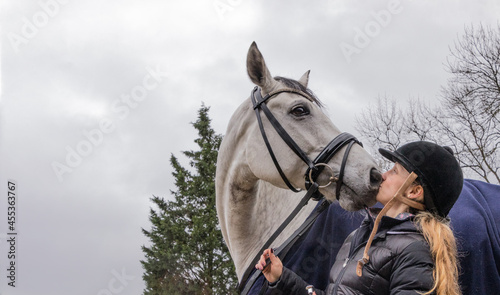 Pferdeliebe: weisses Pferd küsst blonde Reiterin mit Helm im Winter