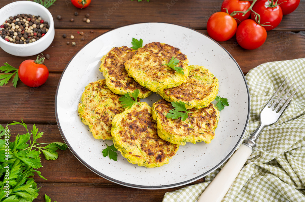 Vegetable zucchini pancakes with cheese, dill and parsley on a plate with sour cream on a dark wooden background. copy space Vegetable zucchini pancakes with cheese, dill and parsley on a plate with sour cream on a dark wooden background. copy space