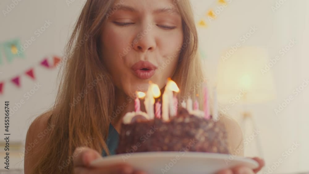 Happy birthday to me. Young cheerful woman blowing up candles on her birthday cake and smiling widely, tracking shot