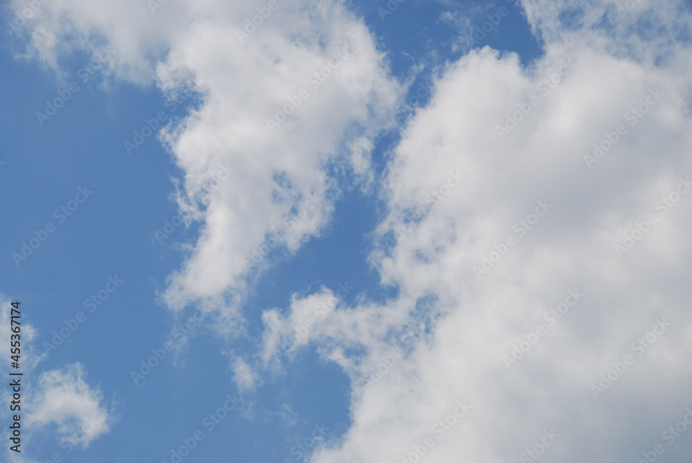 Fototapeta premium Light white fluffy clouds. Against the background of a light blue sky, a snow-white cloud in a light solar haze. A cloud surrounds the blue of the sky.