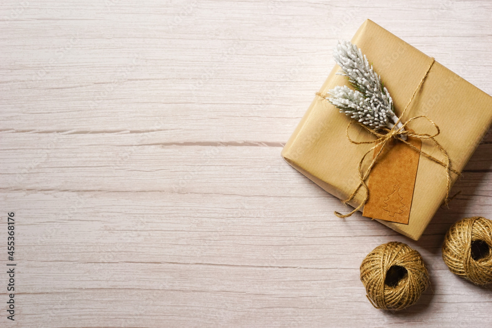 Christmas present wrapped in natural brown paper on light wooden background. Sustainable holiday gift wrapping concept. Merry Christmas. Modern natural decoration. Empty space for text. Copy space.