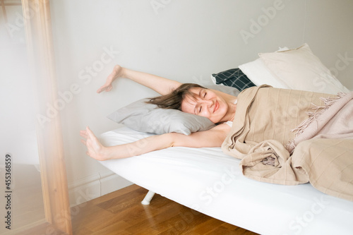 Young beautiful caucasian woman wakes up in the morning. Woman is basking in her bed.