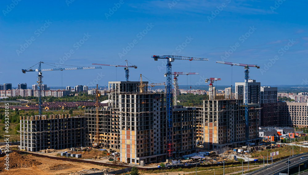 Construction cranes and houses under construction. Construction of a new high-rise buildings in residential district