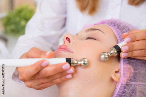 Woman in a spa salon on cosmetic procedures for facial care. Cosmetologist making a woman a therapeutic procedure on a face. Beautician makes medical procedures using a professional equipment.