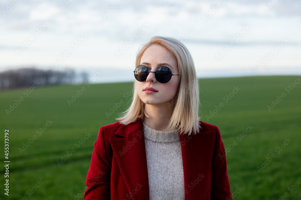 Style blonde woman in sunglasses and red coat at countryside