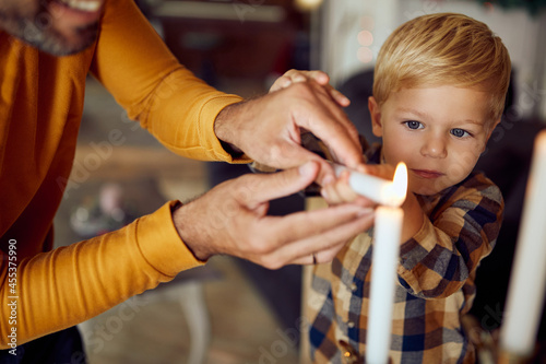 Little boy and his father lighting menorah candles while celebrating Hanukkah at home. photo