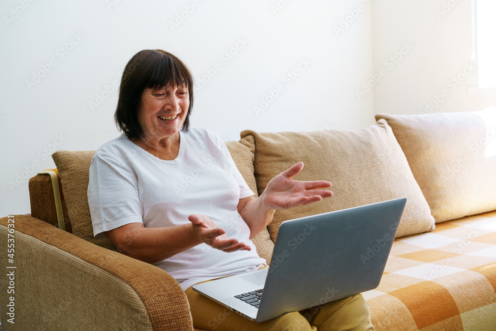 Elderly mature woman using wireless laptop apps browsing internet sitting on sofa smiling middle aged grandmother working on computer surfing internet chatting online looking at screen at home Elderly mature woman using wireless laptop apps browsing internet sitting on sofa smiling middle aged grandmother working on computer surfing internet chatting online looking at screen at home