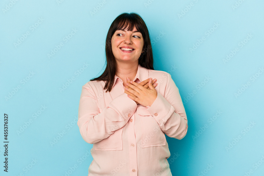 Young curvy caucasian woman isolated on blue background laughing keeping hands on heart, concept of happiness. Young curvy caucasian woman isolated on blue background laughing keeping hands on heart, concept of happiness.