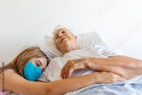 Mulher idosa doente de cama após queda com braço quebrado recebe carinho de neta no leito  photo