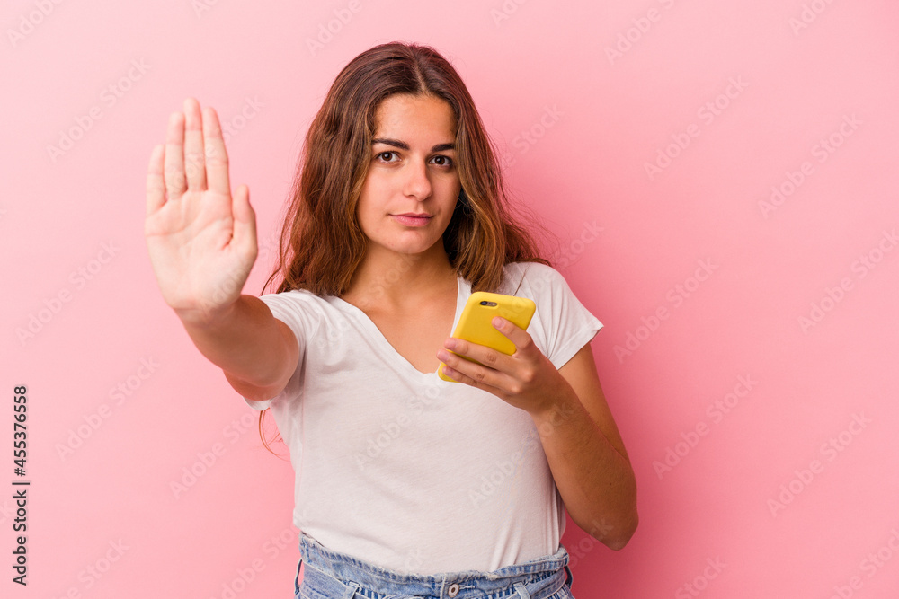 Young caucasian woman using mobile phone isolated on pink background standing with outstretched hand showing stop sign, preventing you. Young caucasian woman using mobile phone isolated on pink background standing with outstretched hand showing stop sign, preventing you.