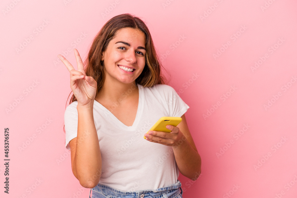 Young caucasian woman using mobile phone isolated on pink background showing number two with fingers. Young caucasian woman using mobile phone isolated on pink background showing number two with fingers.