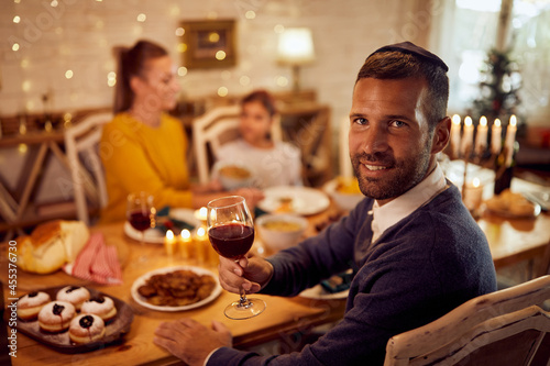 Happy Jewish man drinks wine while having meal with his family on Hanukkah.