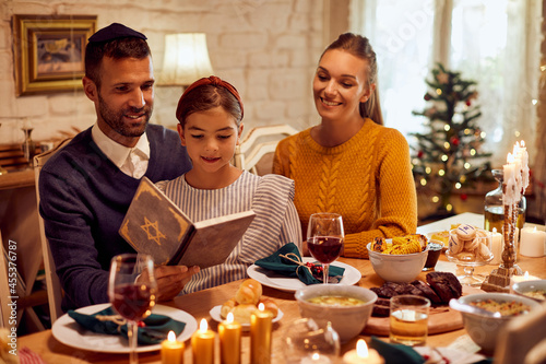 Happy family reads Hebrew bible during traditional Hanukkah meal at dining table.