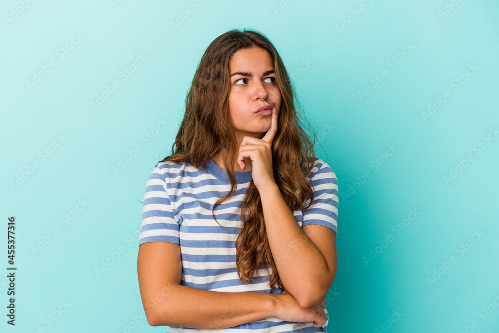 Young caucasian woman isolated on blue background  looking sideways with doubtful and skeptical expression.