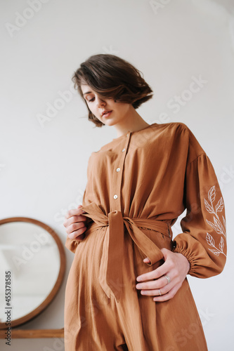 Konstfotografi Upward angle image of sexy woman in a brown jumpsuit tightening her belt bow