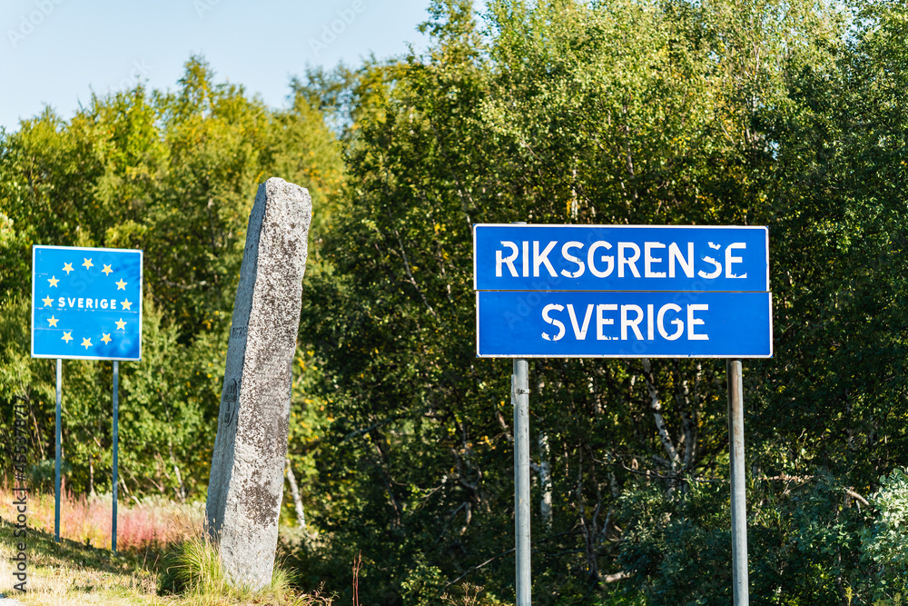 Fototapeta premium State border between Norway and Sweden in Northern Sweden, mountains in Lappland. Mile stone with Swedish text and blur road sign with Norwegian words, European Union road sign on Swedish