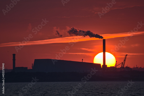 Beautiful telephoto view of epic orange sunset over Dublin port and Sun aligned with Covanta Plant (Dublin Waste to Energy) seen from west pier of Dun Laoghaire harbor, Dublin, Ireland. Soft focus