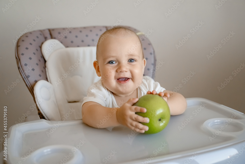 a baby with blue eyes in a high chair with a green apple, smiling a baby with blue eyes in a high chair with a green apple, smiling