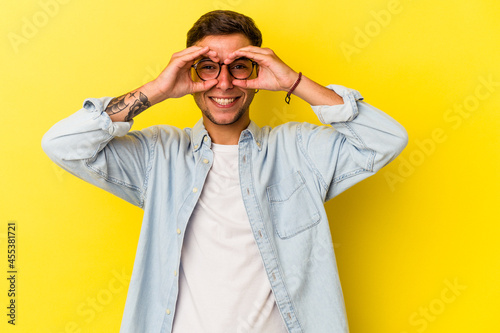 Young caucasian man with tattoos isolated on yellow background  showing okay sign over eyes © Asier