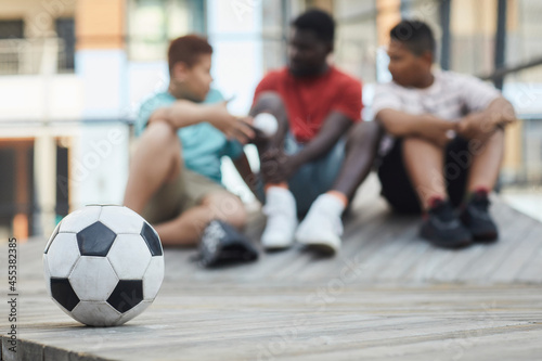Focus on soccer ball on wooden podium outdoors, black father talking to sons in background