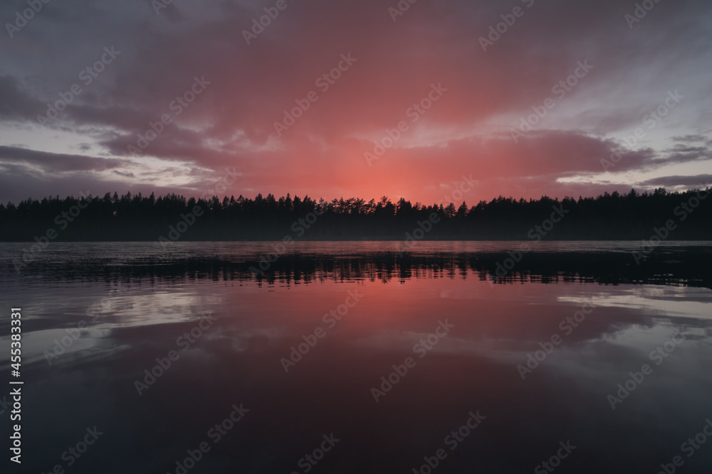 A cloud illuminated by the setting sun over a picturesque forest lake