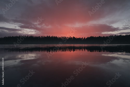 A cloud illuminated by the setting sun over a picturesque forest lake