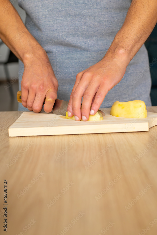 close up of a man cutting a peeled potato in dices on a wood cutting board