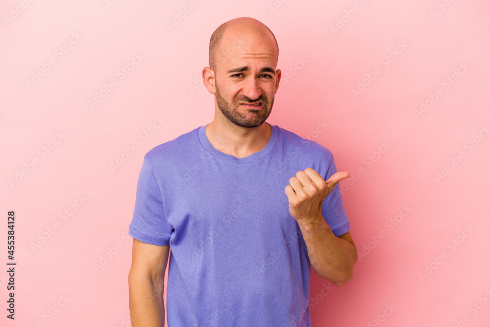 Young caucasian bald man isolated on pink background shocked pointing with index fingers to a copy space. Young caucasian bald man isolated on pink background shocked pointing with index fingers to a copy space.