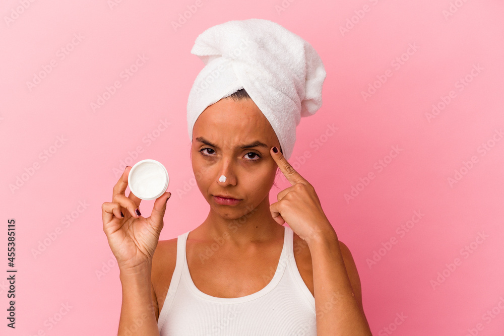 Young mixed race woman holding facial cream isolated on pink background pointing temple with finger, thinking, focused on a task. Young mixed race woman holding facial cream isolated on pink background pointing temple with finger, thinking, focused on a task.