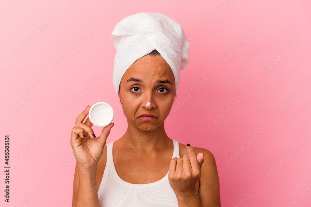 Young mixed race woman holding facial cream isolated on pink background pointing with finger at you as if inviting come closer. Young mixed race woman holding facial cream isolated on pink background pointing with finger at you as if inviting come closer.