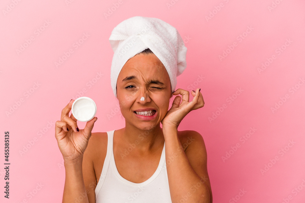 Young mixed race woman holding facial cream isolated on pink background covering ears with hands. Young mixed race woman holding facial cream isolated on pink background covering ears with hands.