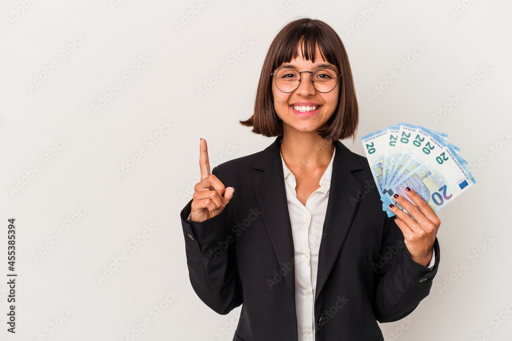 Young mixed race business woman holding a banknotes isolated on white background showing number one with finger. Young mixed race business woman holding a banknotes isolated on white background showing number one with finger.