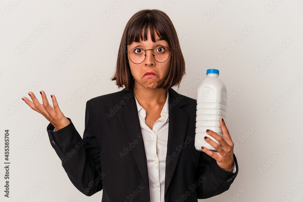 Young mixed race business woman holding a milk bottle isolated on white background shrugs shoulders and open eyes confused. Young mixed race business woman holding a milk bottle isolated on white background shrugs shoulders and open eyes confused.